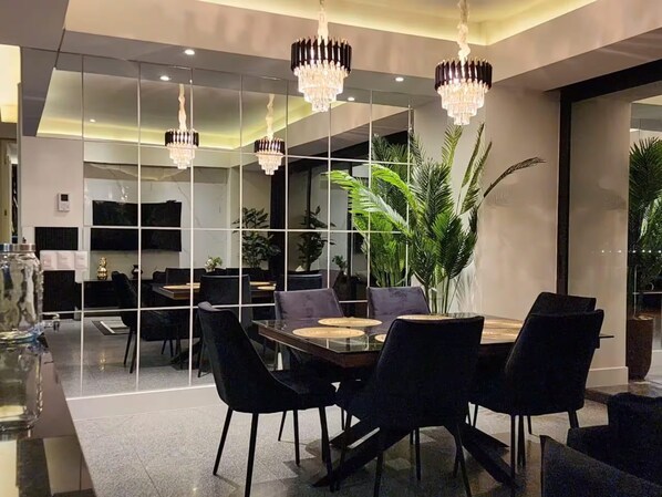 A modern dining area with a glass table, black chairs, and a large potted plant.