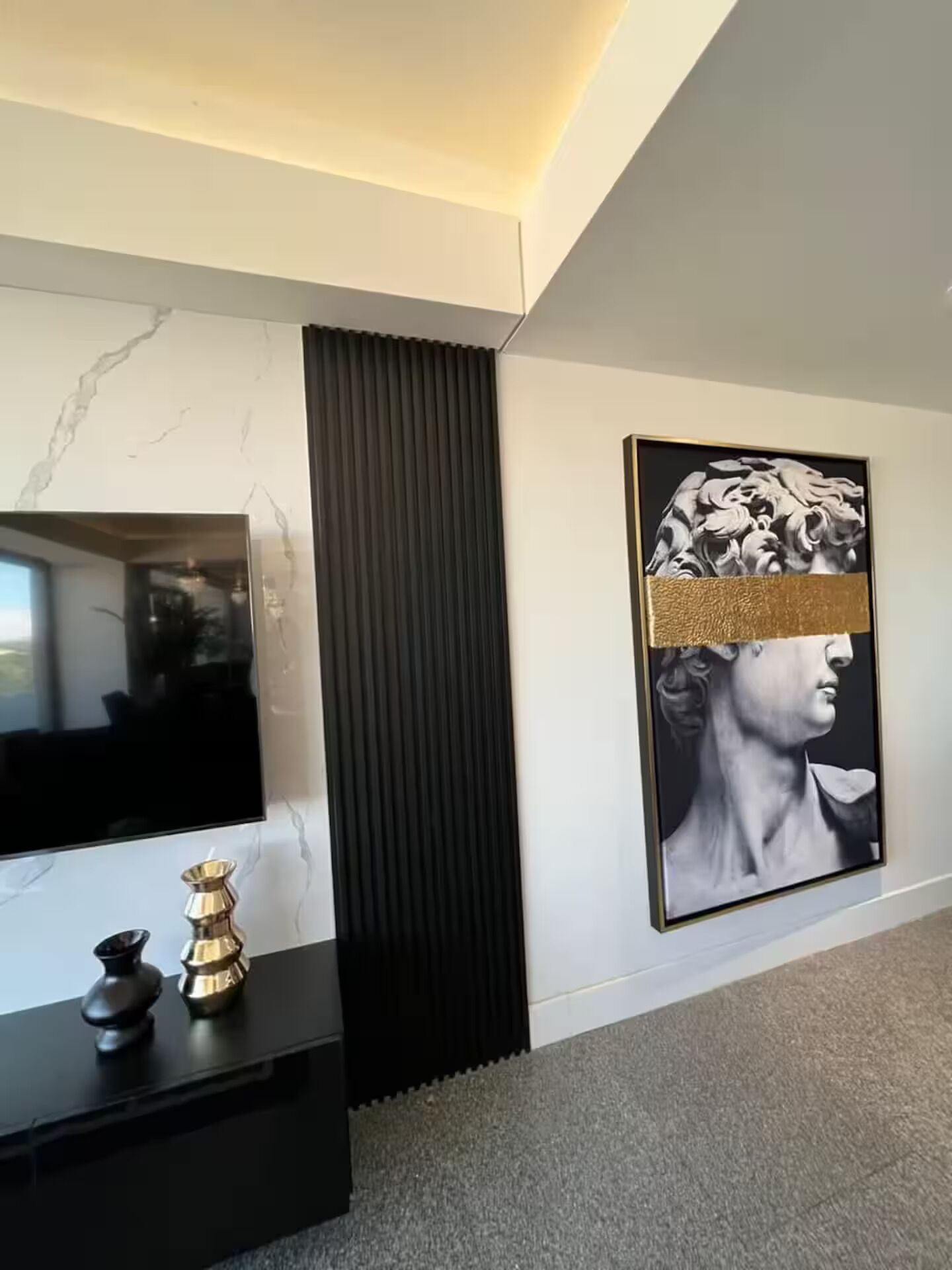 Un interior moderno con una pared de mármol, un panel vertical negro, una obra de arte enmarcada y una consola negra con objetos decorativos.