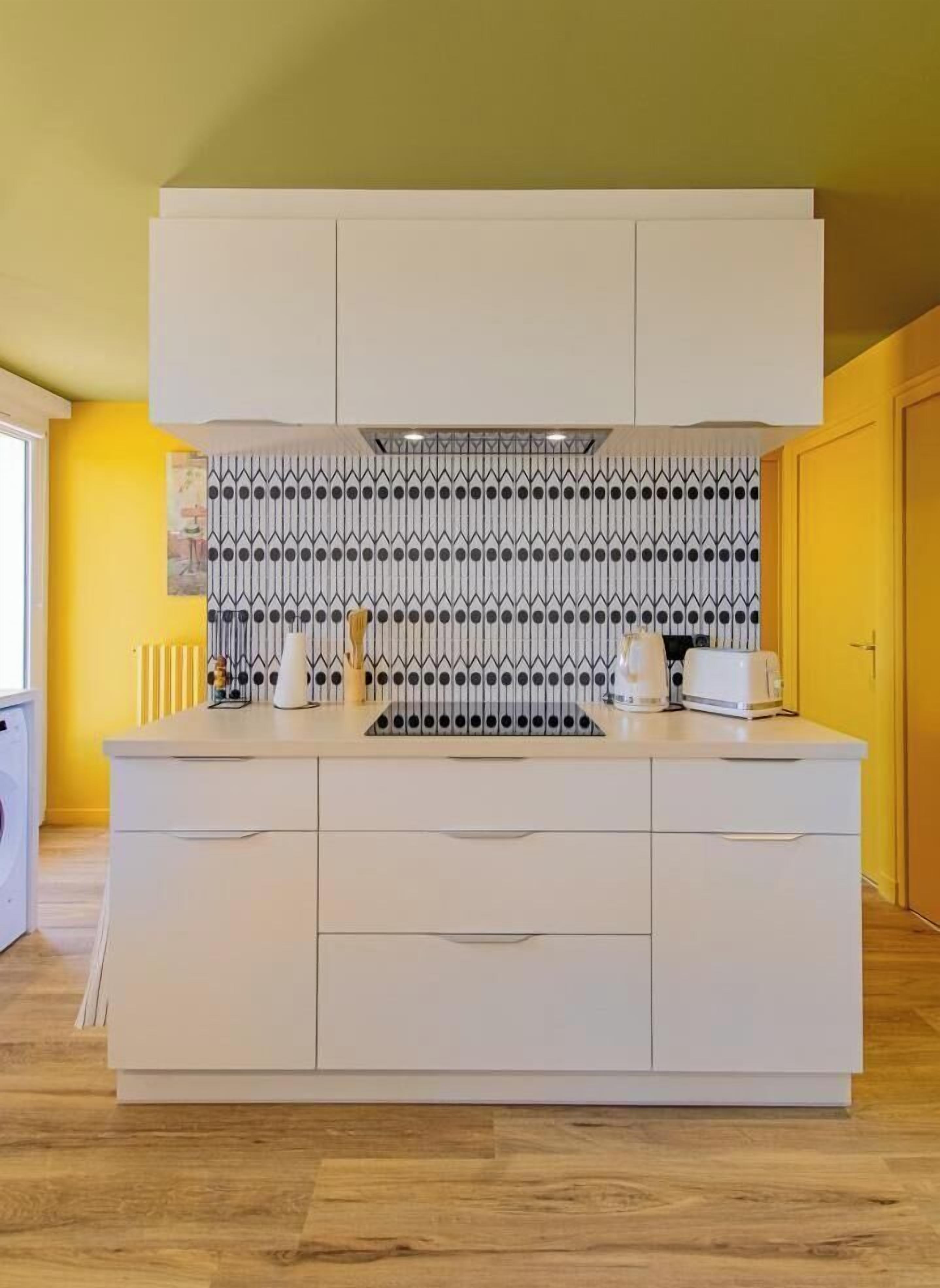 A modern kitchen with a white countertop, a patterned backsplash, and a yellow wall.