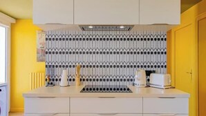 Uma cozinha moderna com bancada branca, painel de fundo padronizado e parede amarela.