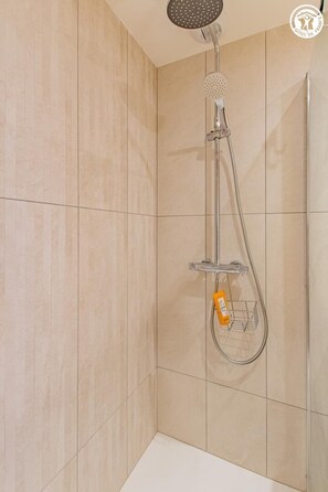 Eine Dusche mit Duschbrause, Wandarmatur und Seifenspender.