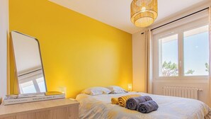 Quarto com cama, mesa de cabeceira, espelho e janela.