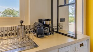 Uma cozinha compacta com máquina de lavar, cafeteira e janela com vista.