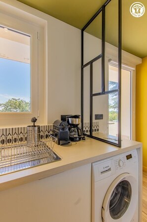 Eine kompakte Küche mit Waschmaschine, Kaffeemaschine und einem Fenster mit Blick.