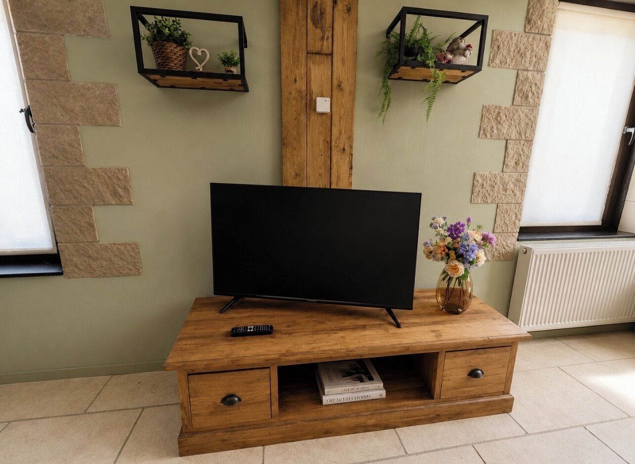 Een houten entertainmentkast met een flatscreentelevisie, een afstandsbediening en een vaas met bloemen.