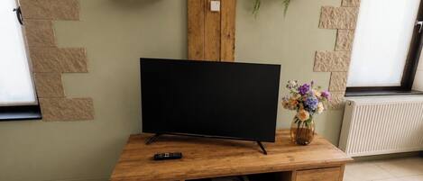 Een houten entertainmentkast met een flatscreentelevisie, een afstandsbediening en een vaas met bloemen.