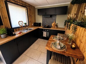 A modern kitchen with black cabinets, a wooden countertop, a built-in oven, and a dining area set for two. - The Durbuy Quarry (Durbuy)