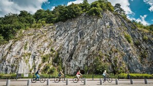 Ein gepflasterter Bereich mit Bojen, eine felsige Klippe und Radfahrer.