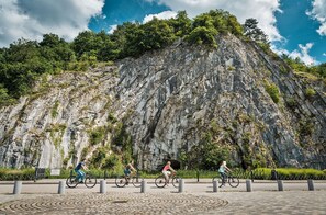 A paved area with bollards, a rocky cliff, and cyclists. - The Durbuy Quarry (Durbuy)