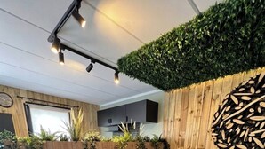 Ein modernes Wohnzimmer mit einem braunen Ledersofa, einer Wand aus Holz mit Grünpflanzen, einem weißen Heizkörper und einer Deckenleuchte.