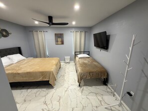 Habitación de hotel con dos camas, ventilador de techo, televisor y piso con diseño de mármol.