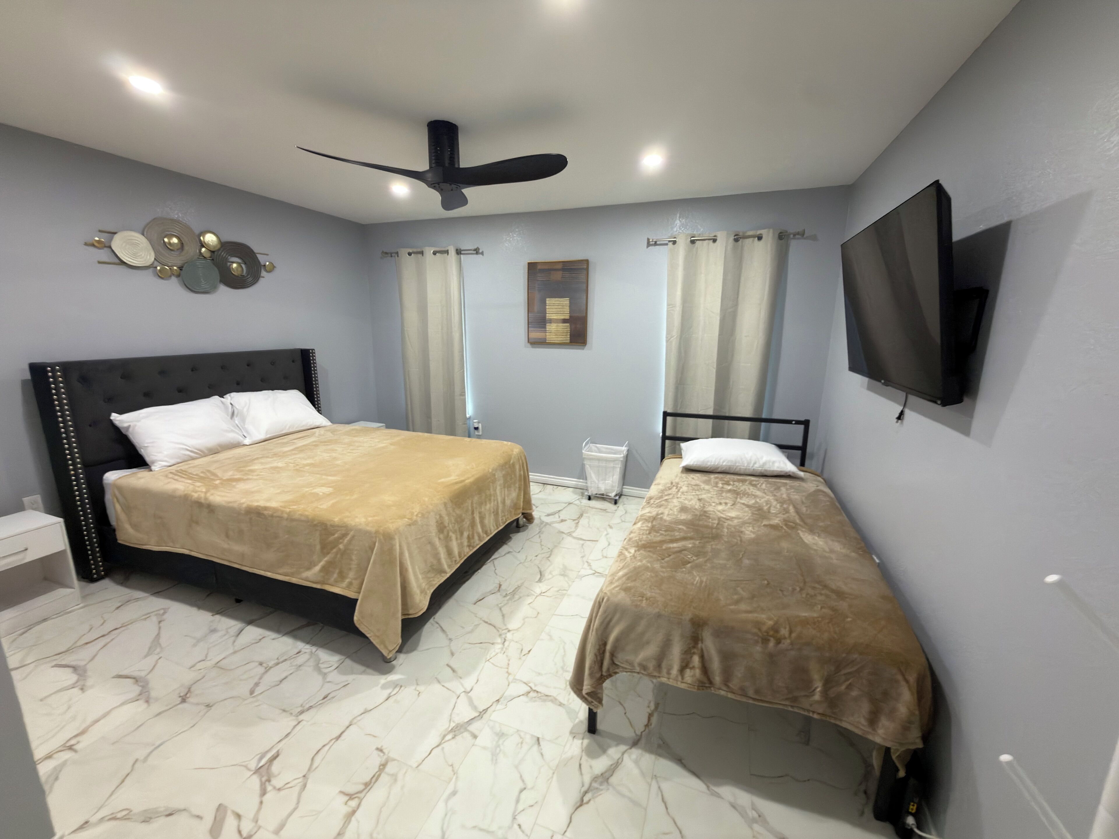 Une chambre avec deux lits, un ventilateur de plafond, une télévision et un sol en marbre.
