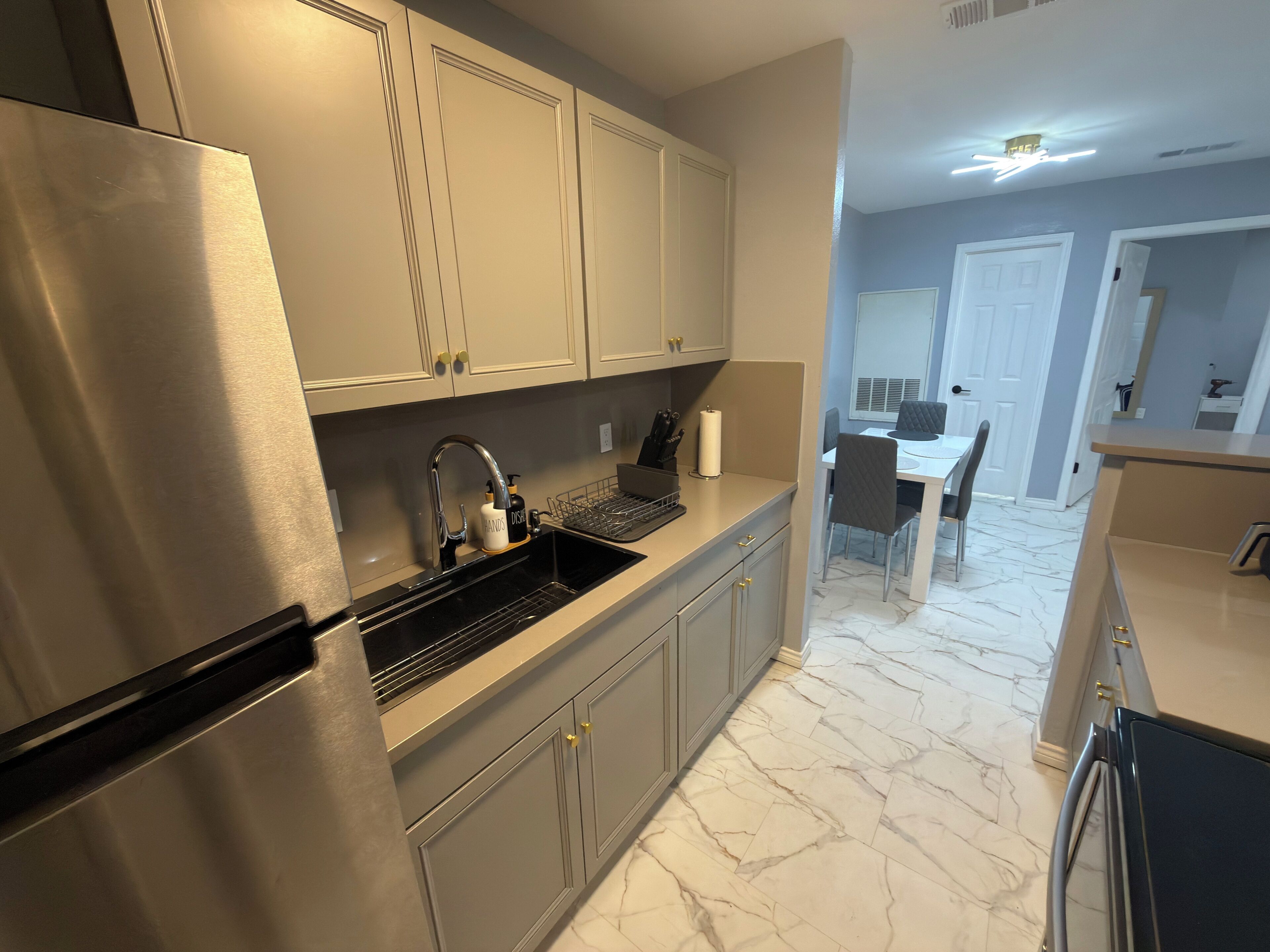 A modern kitchen with stainless steel appliances, marble flooring, and a dining area with a white table and chairs.