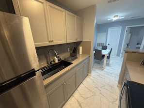 Una cocina moderna con electrodomésticos de acero inoxidable, suelo de mármol y un comedor con mesa y sillas blancas.