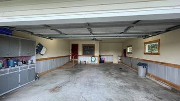 Eine geräumige Garage mit Betonboden, grauen Schränken, einer roten Tür und einem Fenster mit Blick auf Bäume.