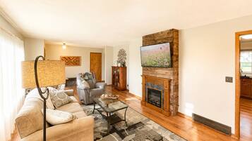 Ein Wohnzimmer mit Sofa, Couchtisch, Kamin, Fernseher und Essbereich.