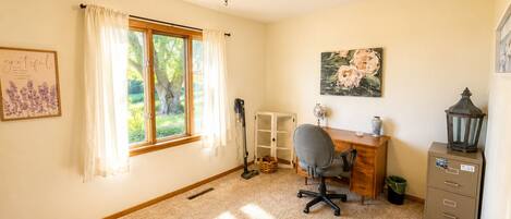 A room with a desk, chair, window with curtains, a radiator, a lamp, a trash bin, and a cabinet.
