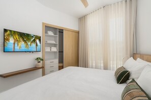 Ein Schlafzimmer mit einem Bett, einem an der Wand montierten Fernseher, einem Kleiderschrank und einem Fenster mit Vorhängen.