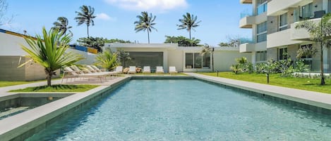 A swimming pool with lounge chairs, palm trees, and a modern building with balconies.