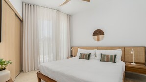 Une chambre avec un grand lit, une table de chevet, une lampe, un grand miroir rond fixé au mur et une plante en pot.