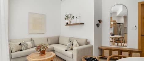Un salon moderne comprenant un canapé, une table basse ronde en bois, un ventilateur de plafond suspendu, une étagère murale agrémentée d’objets décoratifs et un grand miroir qui reflète la pièce.