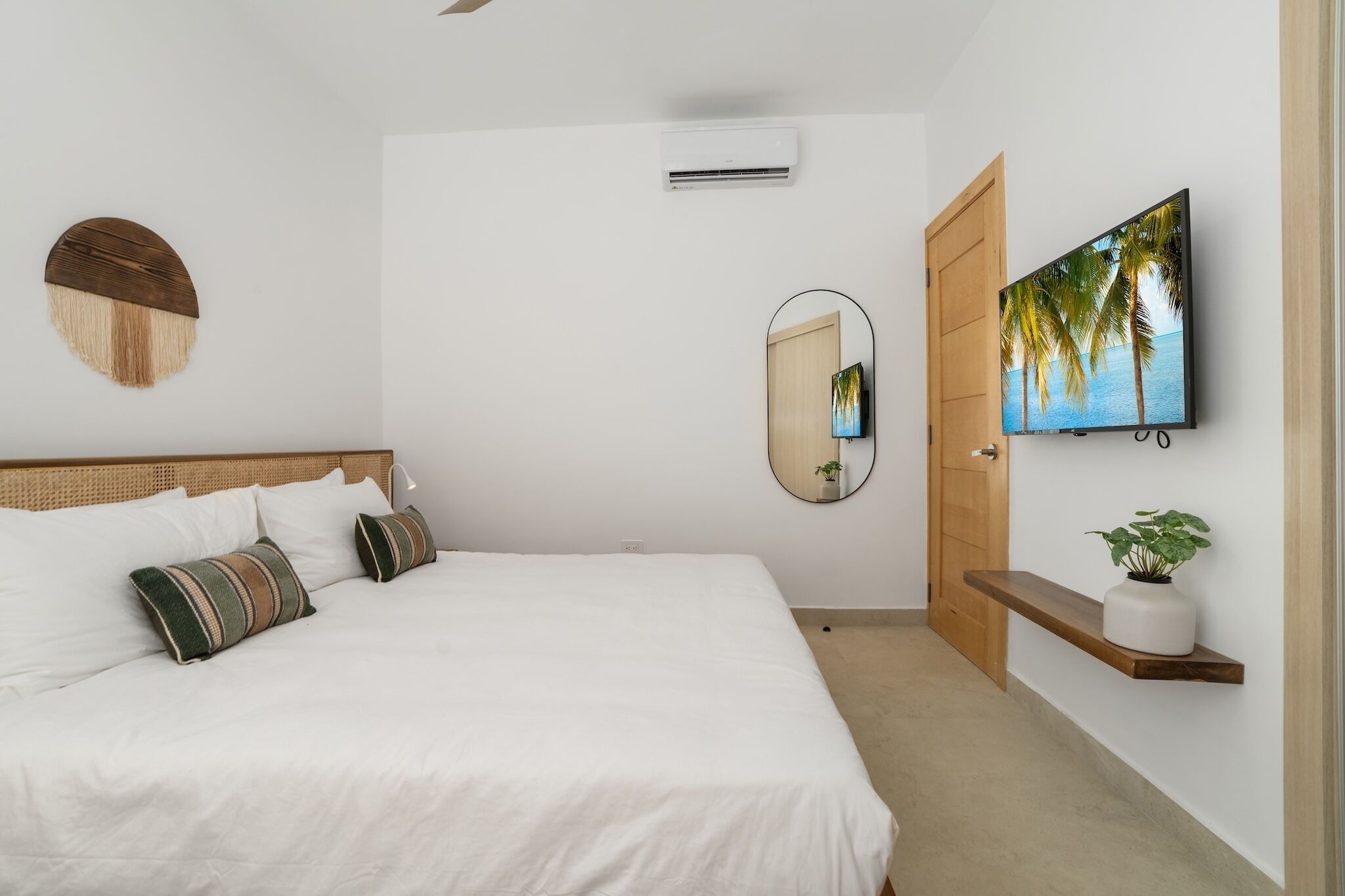 A bedroom with a bed, a wall-mounted air conditioner, a mirror, a television, and a shelf with a plant.