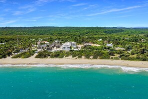Eine Küstenlandschaft mit Strand, einer Wohnsiedlung und einem bewaldeten Hügel im Hintergrund.