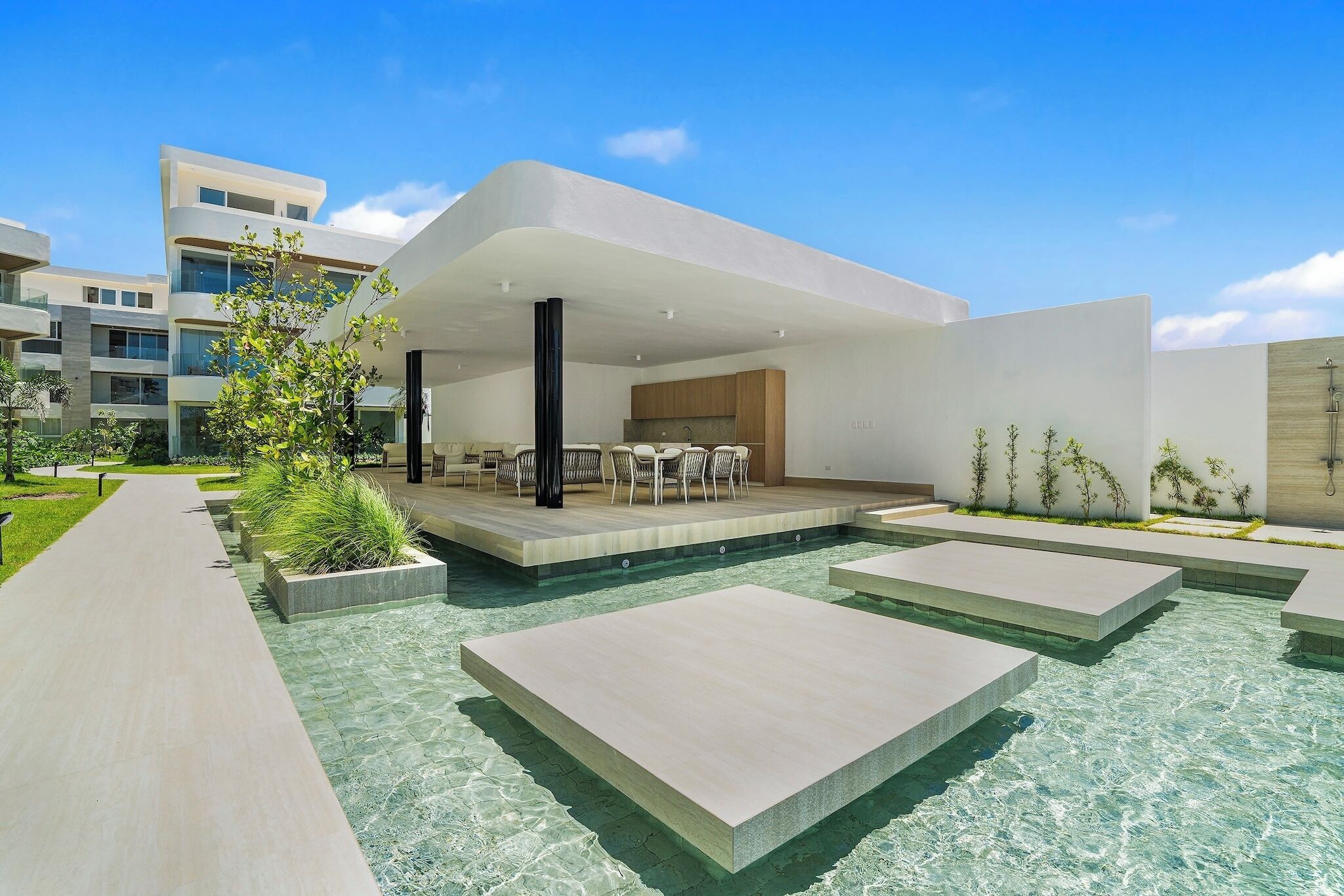 Un área de piscina moderna al aire libre, con zona de comedor y un edificio de techo plano.