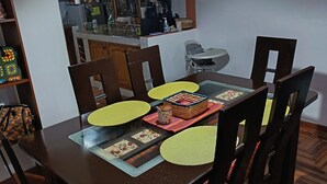 Zona pranzo con tavolo in legno, sedie, una cucina sullo sfondo e una lampada a sospensione.