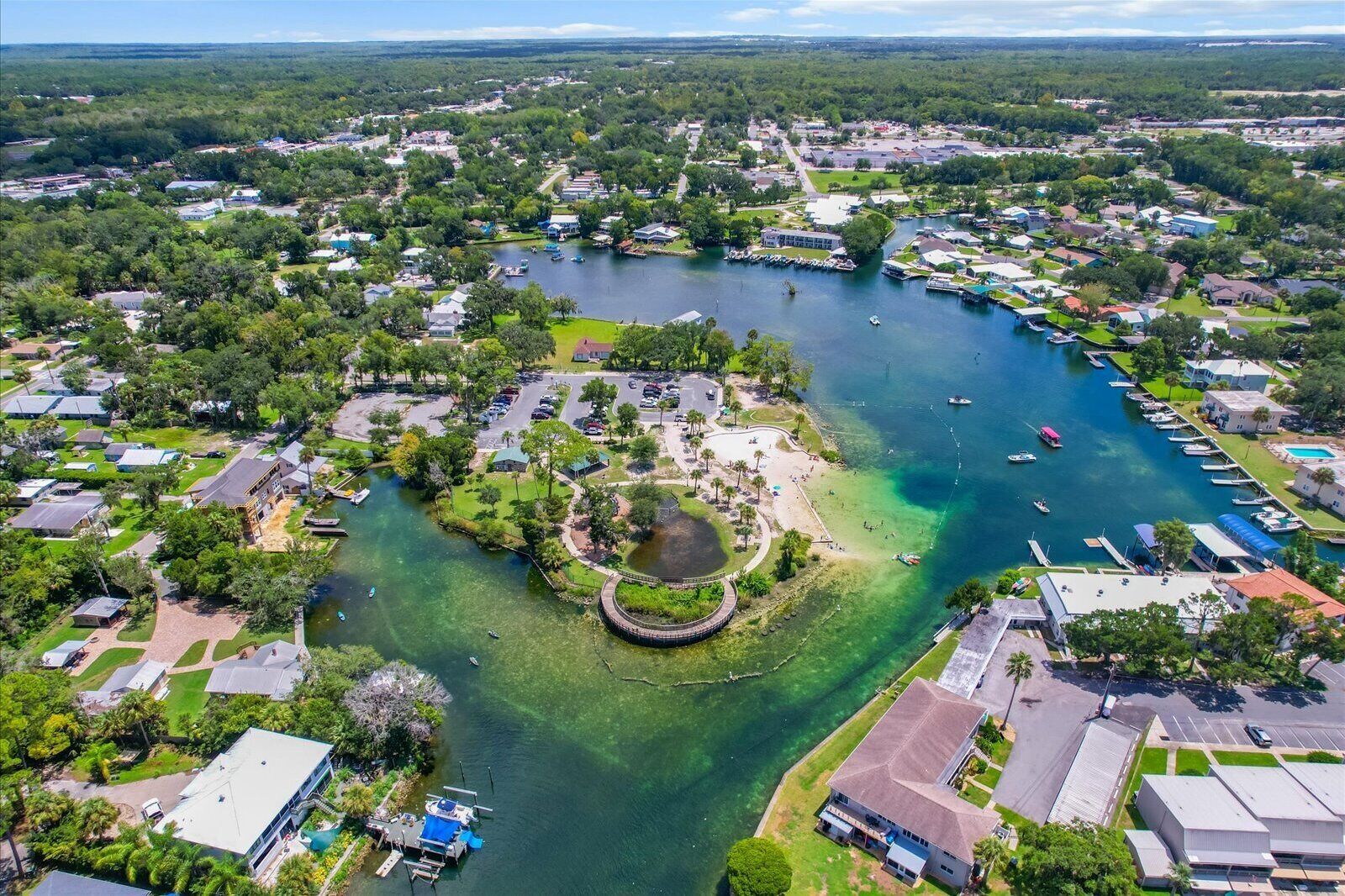 Vista aérea de una comunidad a orillas del lago, con edificios residenciales, un puerto deportivo y un parque central.