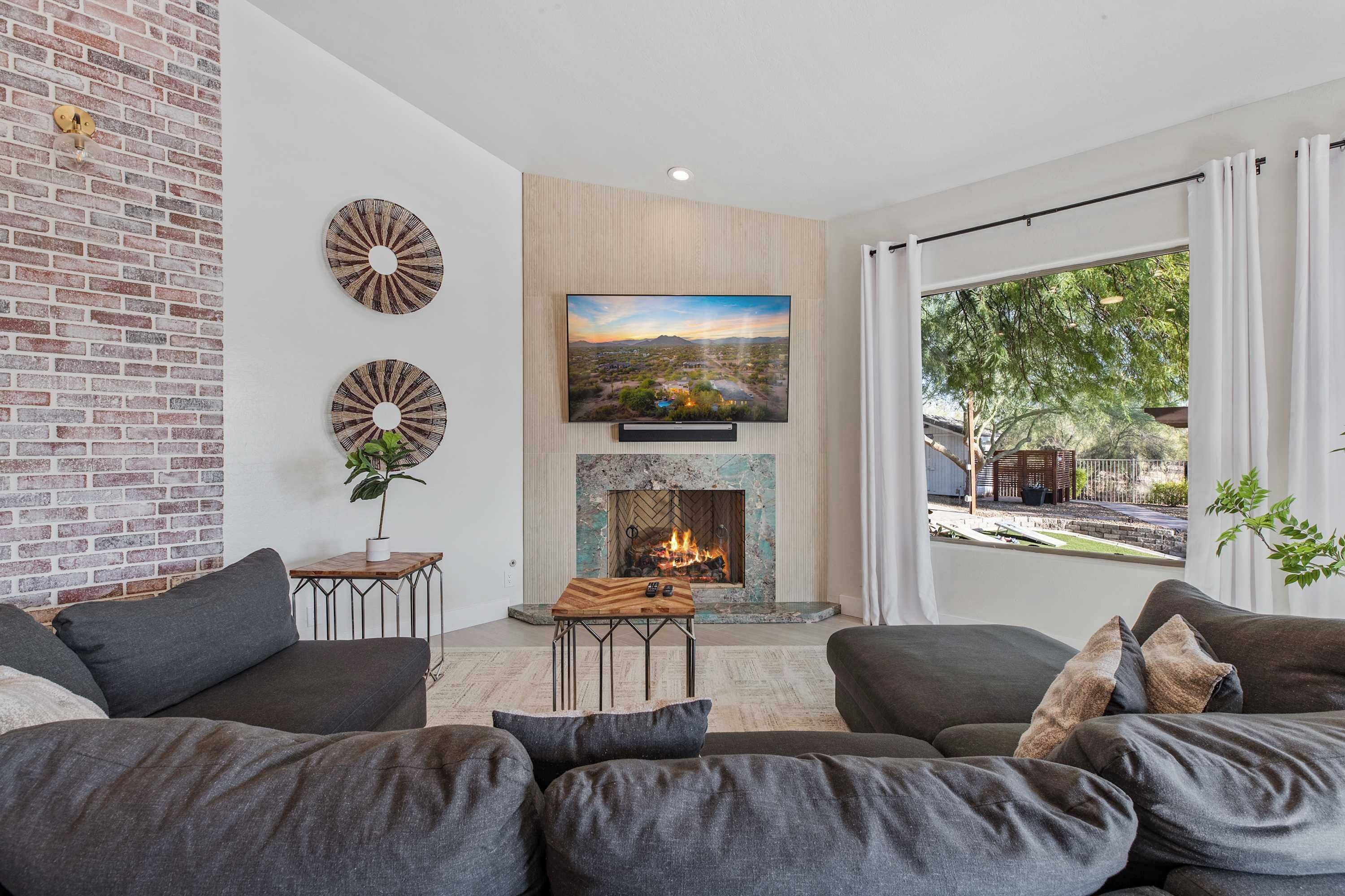 A modern living room with a fireplace, a television mounted above it, and a large window with curtains.