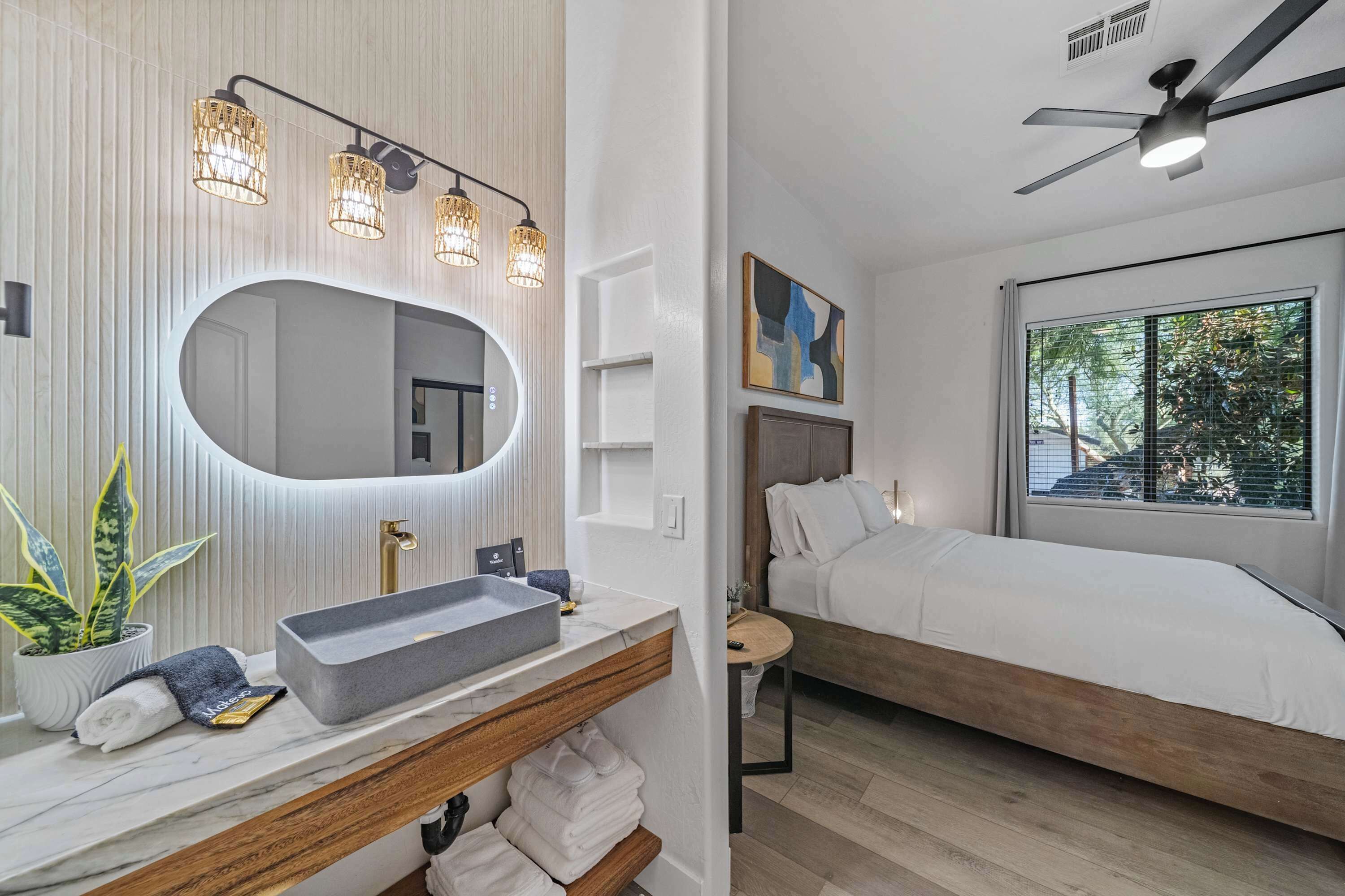 Une salle de bain moderne avec un meuble-lavabo, un évier et un miroir. Il y a un lit avec vue sur l’extérieur.