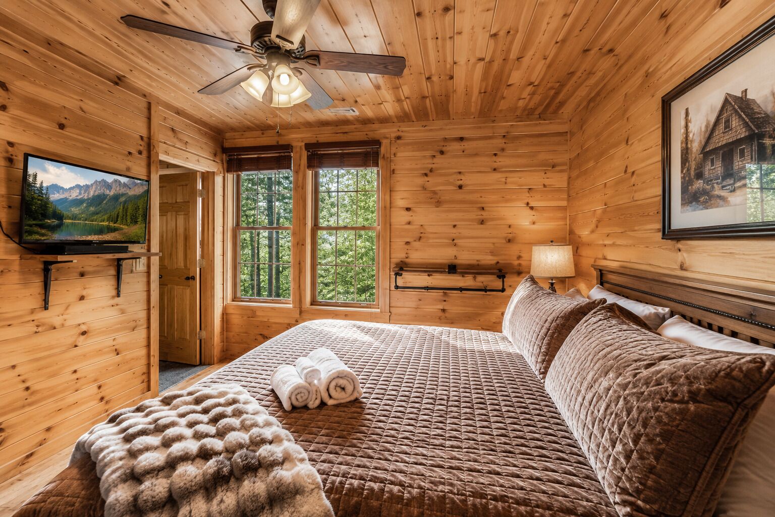 A wooden cabin bedroom with a bed, a ceiling fan, a TV, and a window with a mountain view.