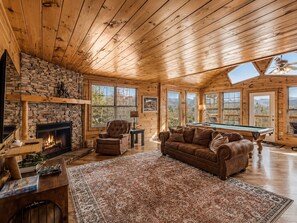 A cozy cabin interior with a fireplace, a pool table, a leather sofa, and a large rug. - Honeymoon VIEW! Beautiful romantic cabin, great location & hot tub w/epic view! (Sevierville)