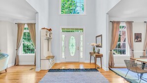 Una habitació àmplia amb un finestra gran, un sòl de fusta, una catifa blava, i una zona de menjador amb taula i cadires.