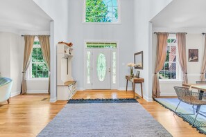 Una habitación amplia con un gran ventanal, suelo de madera, alfombra azul y un comedor con mesa y sillas.
