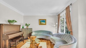 Un saló amb un piano, un sofà corbat, una taula de centre de vidre i un quadre a la paret.