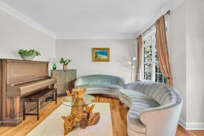 Una sala de estar con un piano, un sofá curvo, una mesa de centro de vidrio y un cuadro en la pared.