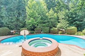 Una piscina con un jacuzzi circular en el centro, rodeado por un suelo de ladrillo y una valla de madera.