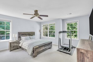 A bedroom with a bed, nightstands, a treadmill, and large windows with a view of greenery. - Private Oasis Retreat with a Pool (Unknown)