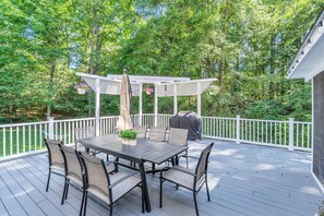 A covered outdoor deck with a table and chairs, surrounded by a white fence and lush greenery. - Private Oasis Retreat with a Pool (Fairfax)