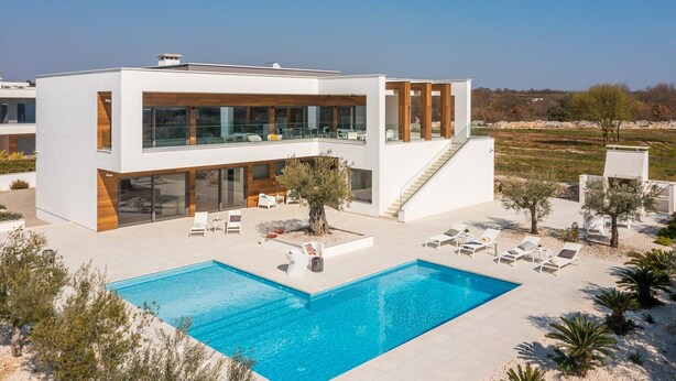 Ein modernes, zweistöckiges Haus mit Swimmingpool, Sitzgelegenheiten im Freien und Blick auf die Landschaft.