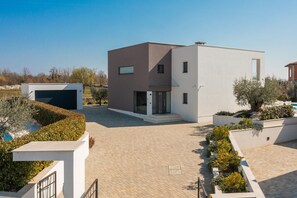 Ein modernes, zweistöckiges Gebäude mit flachem Dach, einer Garage und einem gepflasterten Innenhof.