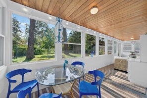 A room with a glass table, blue chairs, a hanging light fixture, and large windows with a view of trees. - New Listing! King Beds, Great Location, Sleeps 6 (Muskegon)