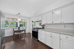 A modern kitchen with white cabinetry, a dining table with chairs, and a large window with a view of greenery. - New Listing! King Beds, Great Location, Sleeps 6 (Muskegon)