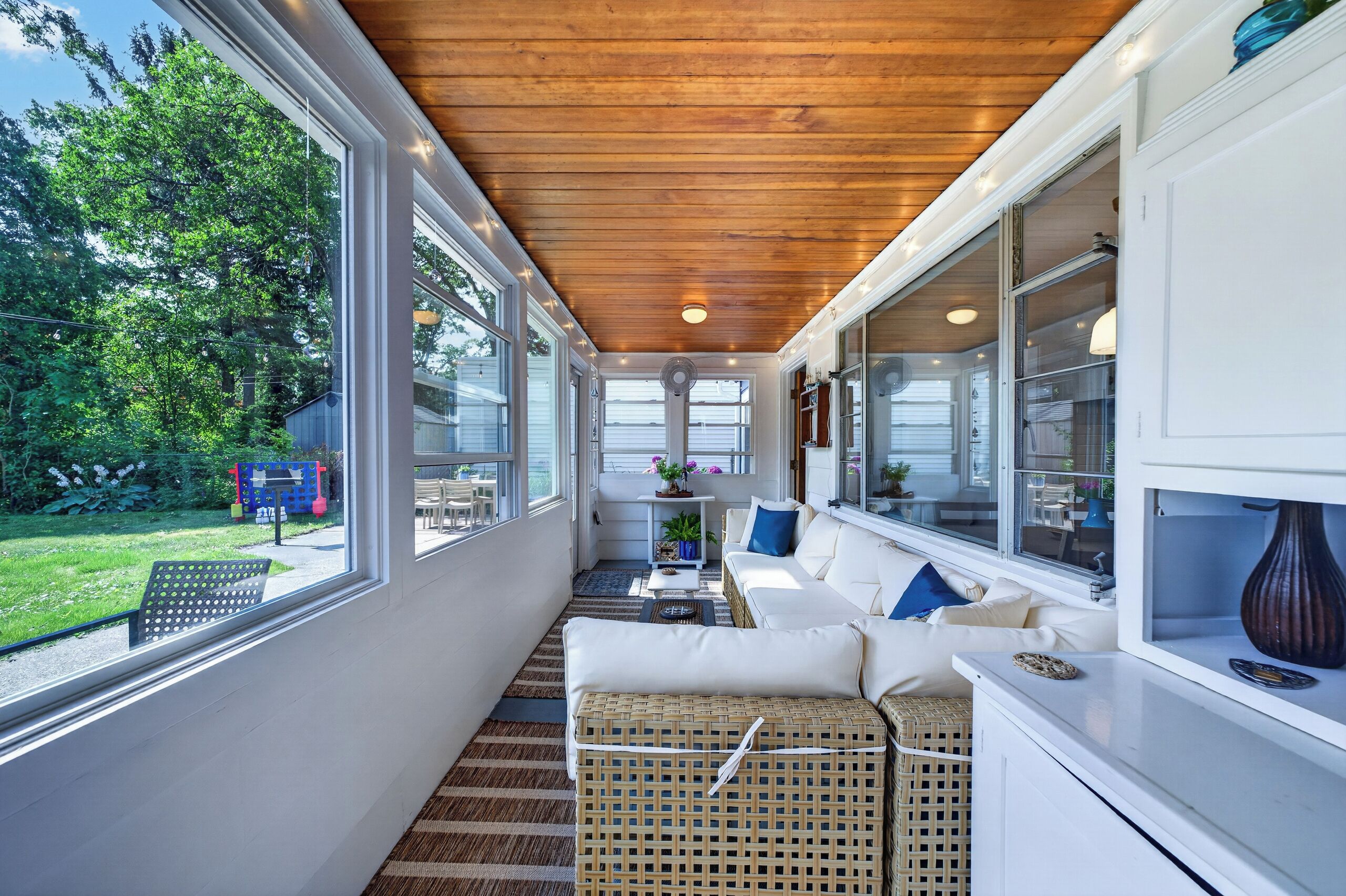 A sunlit room with a wooden ceiling, large windows, and a white sofa with cushions.