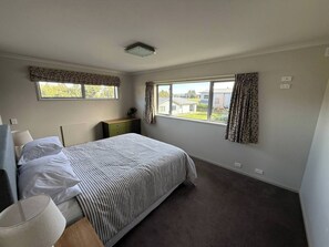 A bedroom with a bed, a dresser, a nightstand, a window with curtains, and a view of the outside. - 53 Snowmass Dr - Ohakune Retreat w/ Ruapehu View (Ohakune)