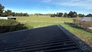 A view from a covered outdoor area with a metal roof, a grassy field, and trees in the background. - 53 Snowmass Dr - Ohakune Retreat w/ Ruapehu View (Ohakune)