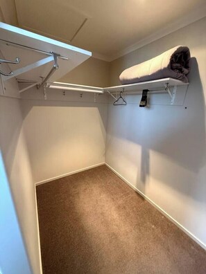 A small, enclosed closet with a hanging rod and a shelf, carpeted floor, and a towel on the shelf. - 53 Snowmass Dr - Ohakune Retreat w/ Ruapehu View (Ohakune)