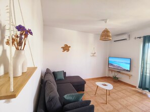 A modern living room with a sofa, a small table, a television, and decorative wall art. - Dream in Paradise - Ocean Views & AC (Corralejo)